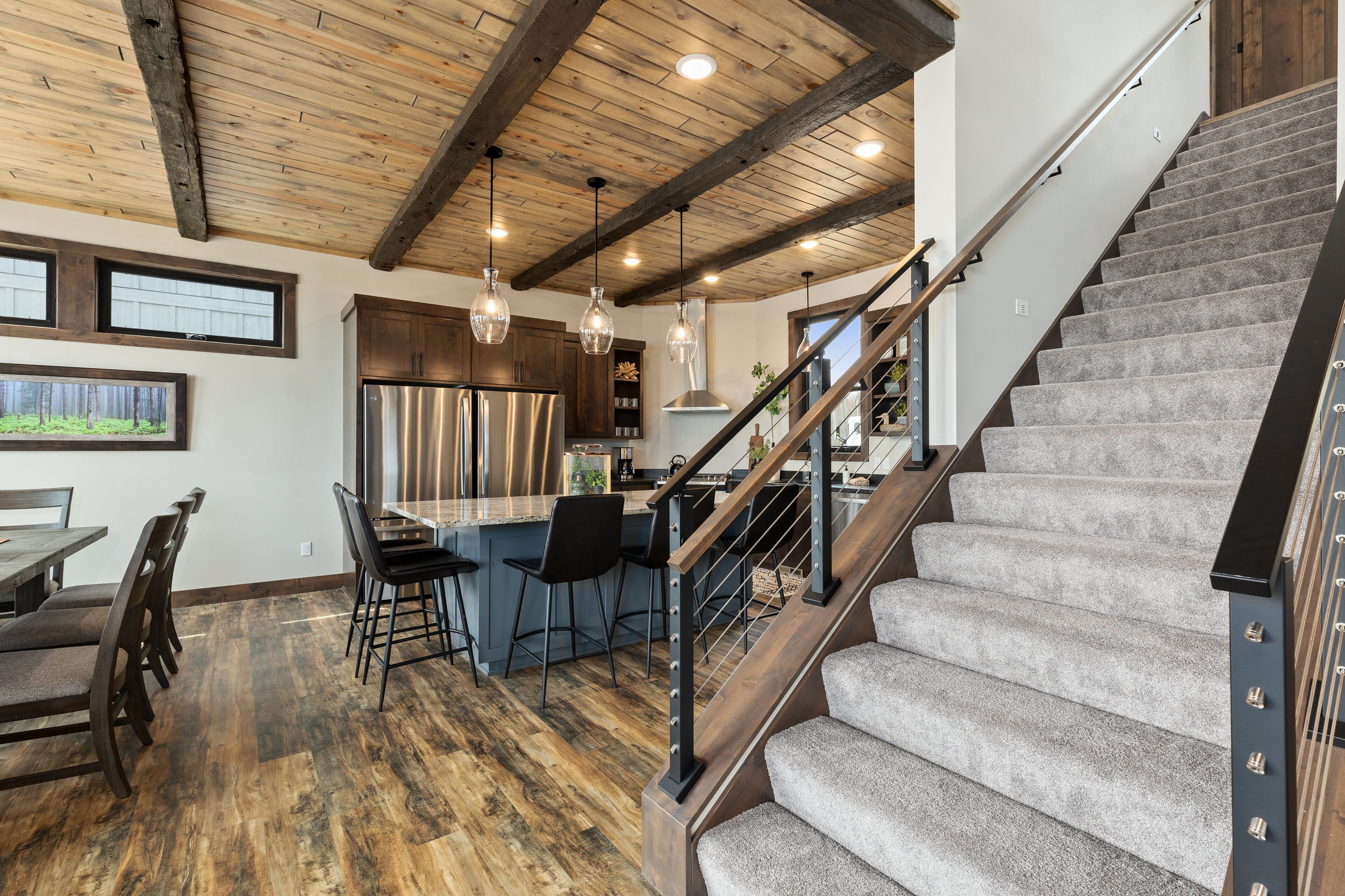 A modern kitchen with a central island, wooden flooring, and a staircase with a grey carpet.