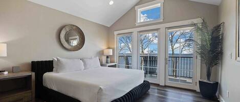A bedroom with a large bed, a round mirror, two bedside tables, and a view of the outdoors through a sliding door.