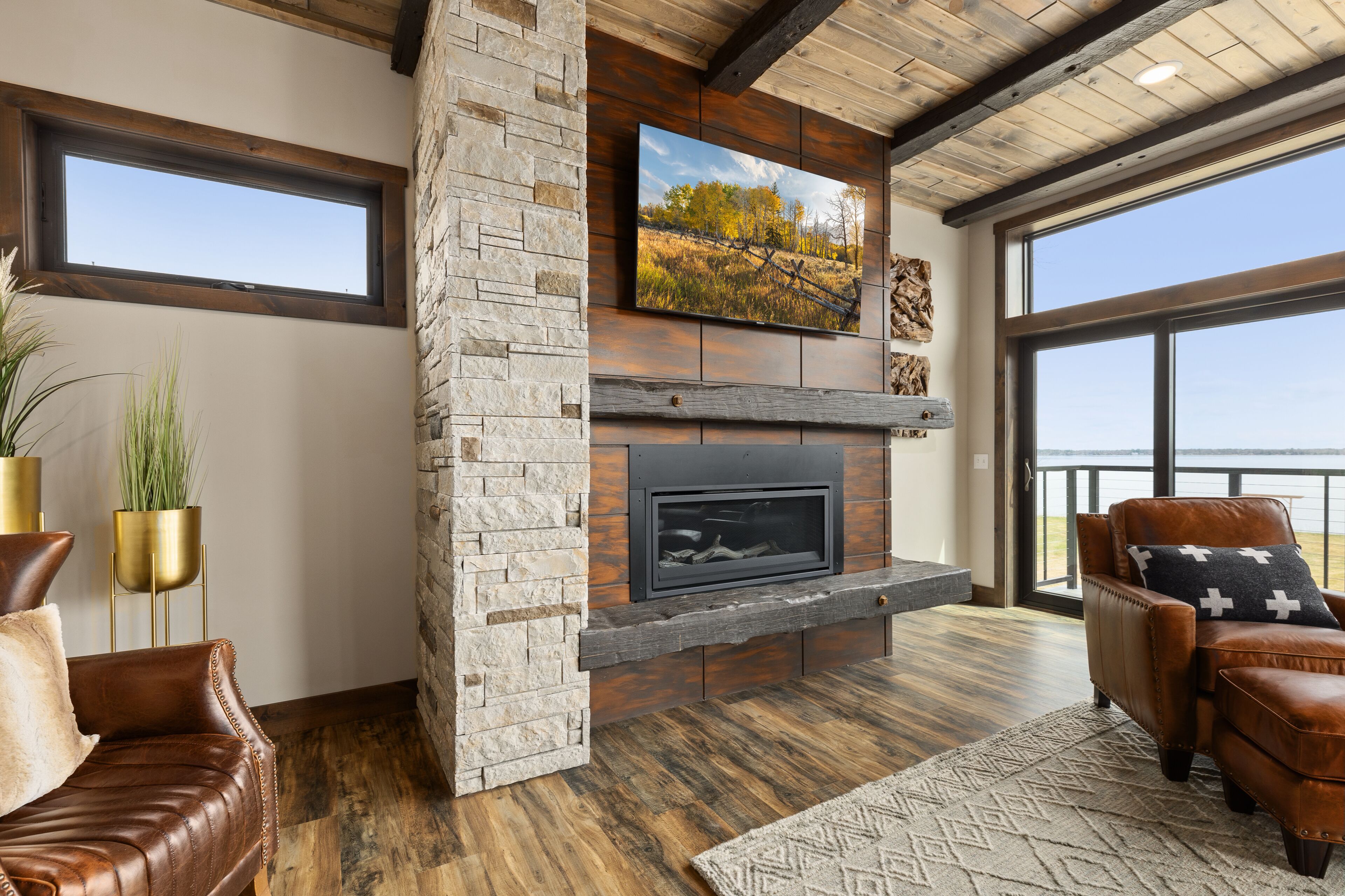 Una sala de estar moderna con chimenea de piedra, sofás de cuero y un gran ventanal con vista al agua.