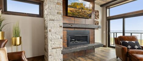 Una sala de estar moderna con chimenea de piedra, sofás de cuero y un gran ventanal con vista al agua.
