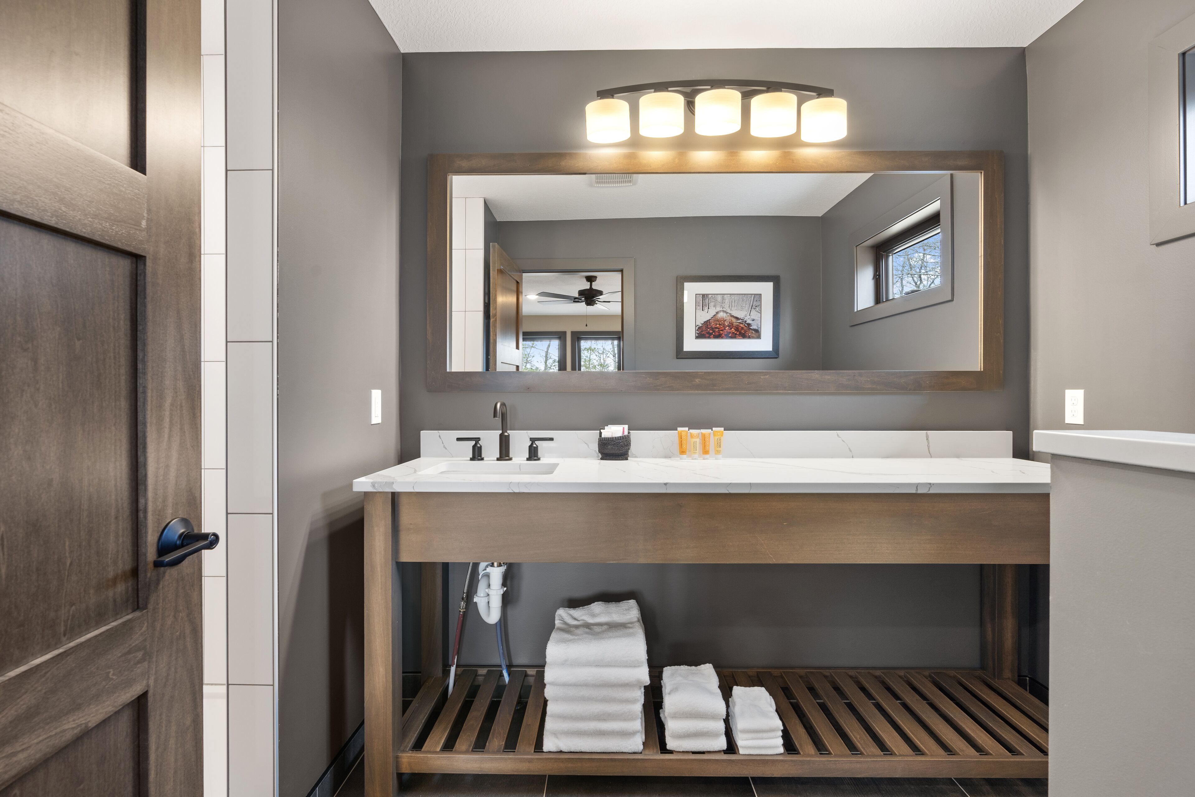 A modern bathroom with a wooden vanity, a large mirror, and a towel rack.