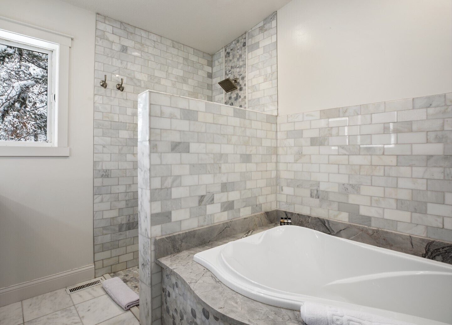 A modern bathroom with a bathtub, a shower area, and a window with a view of trees.