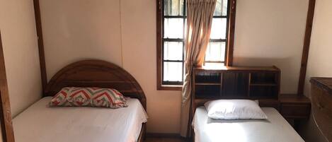 Un dormitorio con dos camas, una ventana con cortinas, un ventilador de techo y un cabecero de madera.