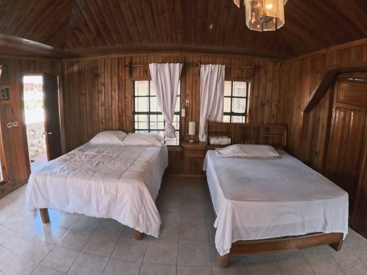 A wooden cabin with two beds, a nightstand, and a hanging light fixture.