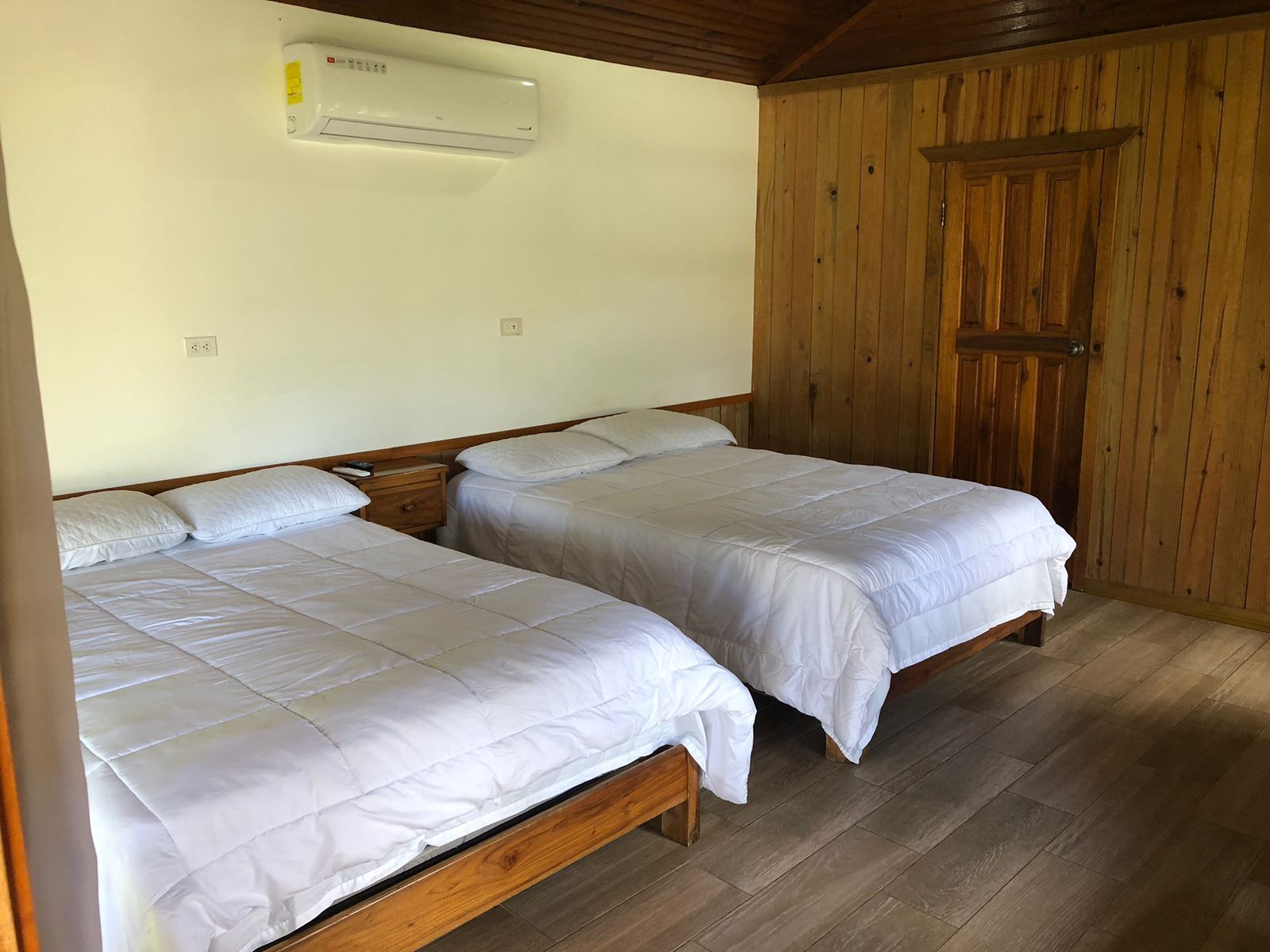 A room with two wooden beds, a wooden wardrobe, and an air conditioning unit on the wall.