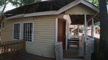 A single-story building with a porch, a wooden fence, and a stone pillar.