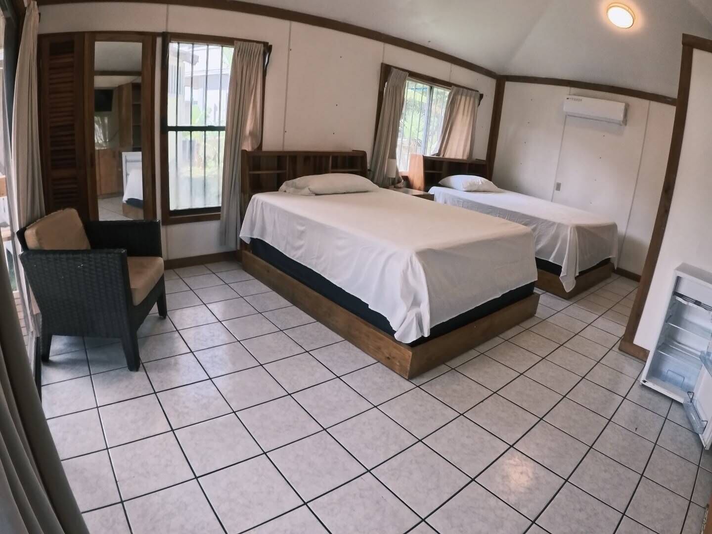 A bedroom with two beds, a chair, and a window.
