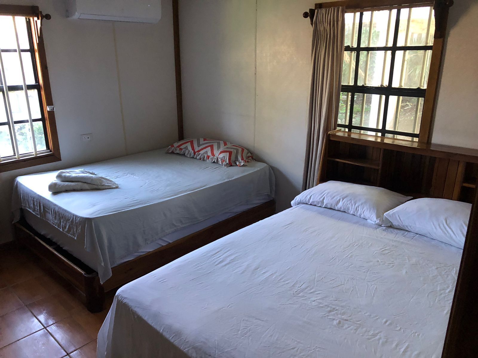 A room with two beds, one with a patterned pillow and the other with plain pillows.