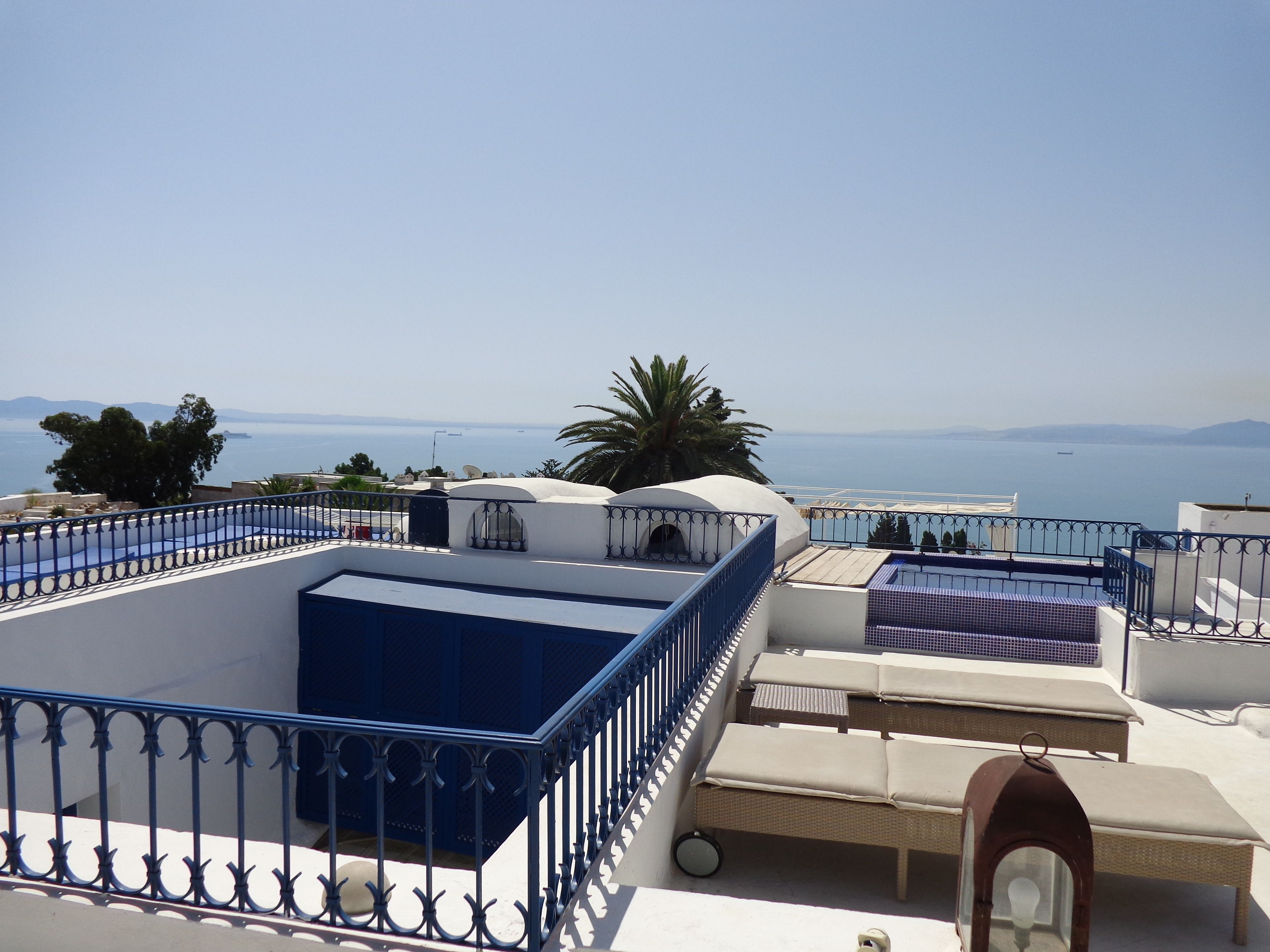 A rooftop terrace with a view of the sea, white walls, and blue railings.
