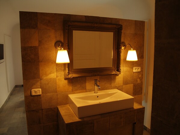 A bathroom with a large mirror, two wall-mounted lamps, and a rectangular sink.