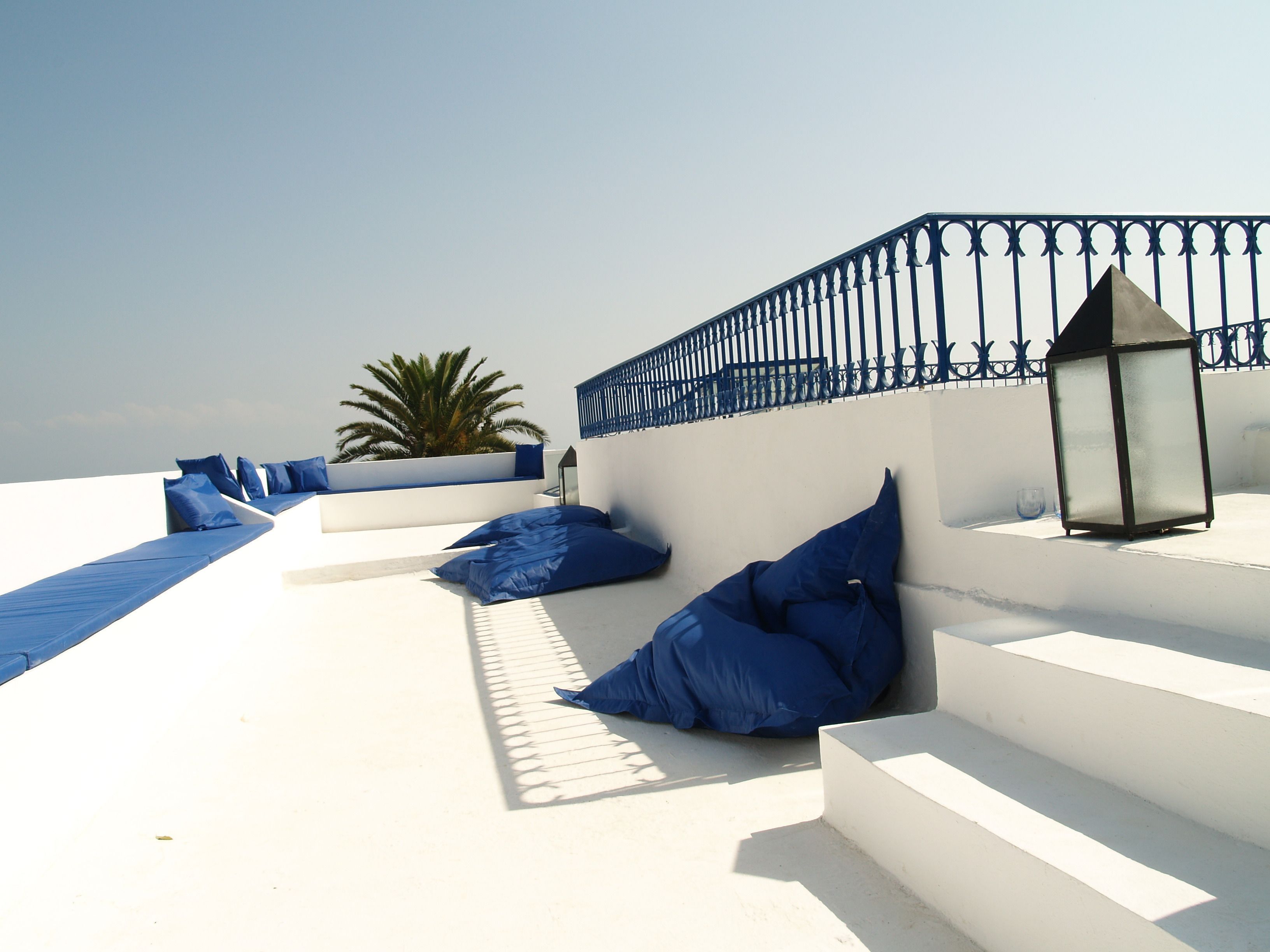 Una terraza exterior blanca con cojines azules y un farol.