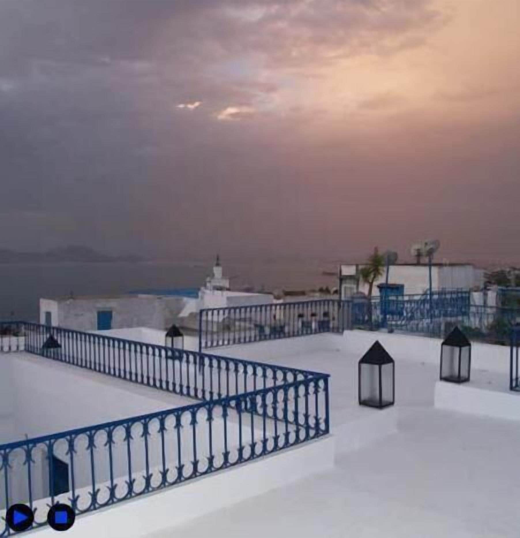 A rooftop terrace with a blue metal railing, white walls, and a view of the city skyline.