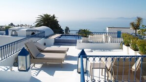 Une terrasse sur le toit, dotée de chaises longues et d’une piscine, offrant une vue panoramique sur le paysage urbain côtier.