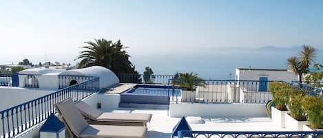 Terraza en la azotea con sillones de descanso y piscina, con vistas a una ciudad costera.