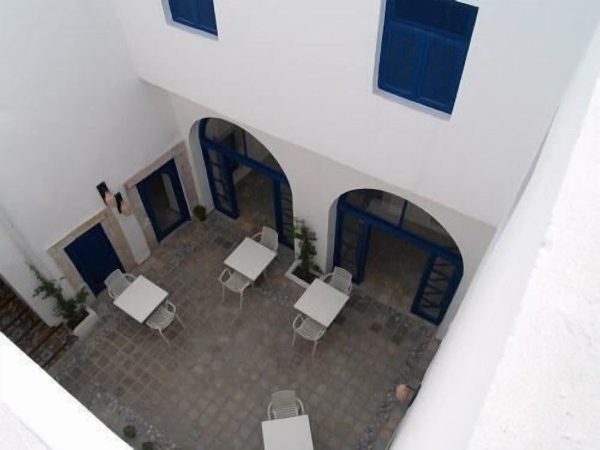 Un patio con paredes blancas, puertas azules y mesas y sillas blancas.