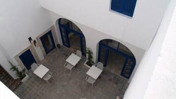 Un patio con paredes blancas, puertas azules y mesas y sillas blancas.