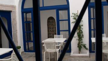 Um pátio com mesas e cadeiras brancas, portas azuis e piso de azulejos.