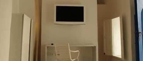 A room with a desk, chair, and a TV mounted on the wall.