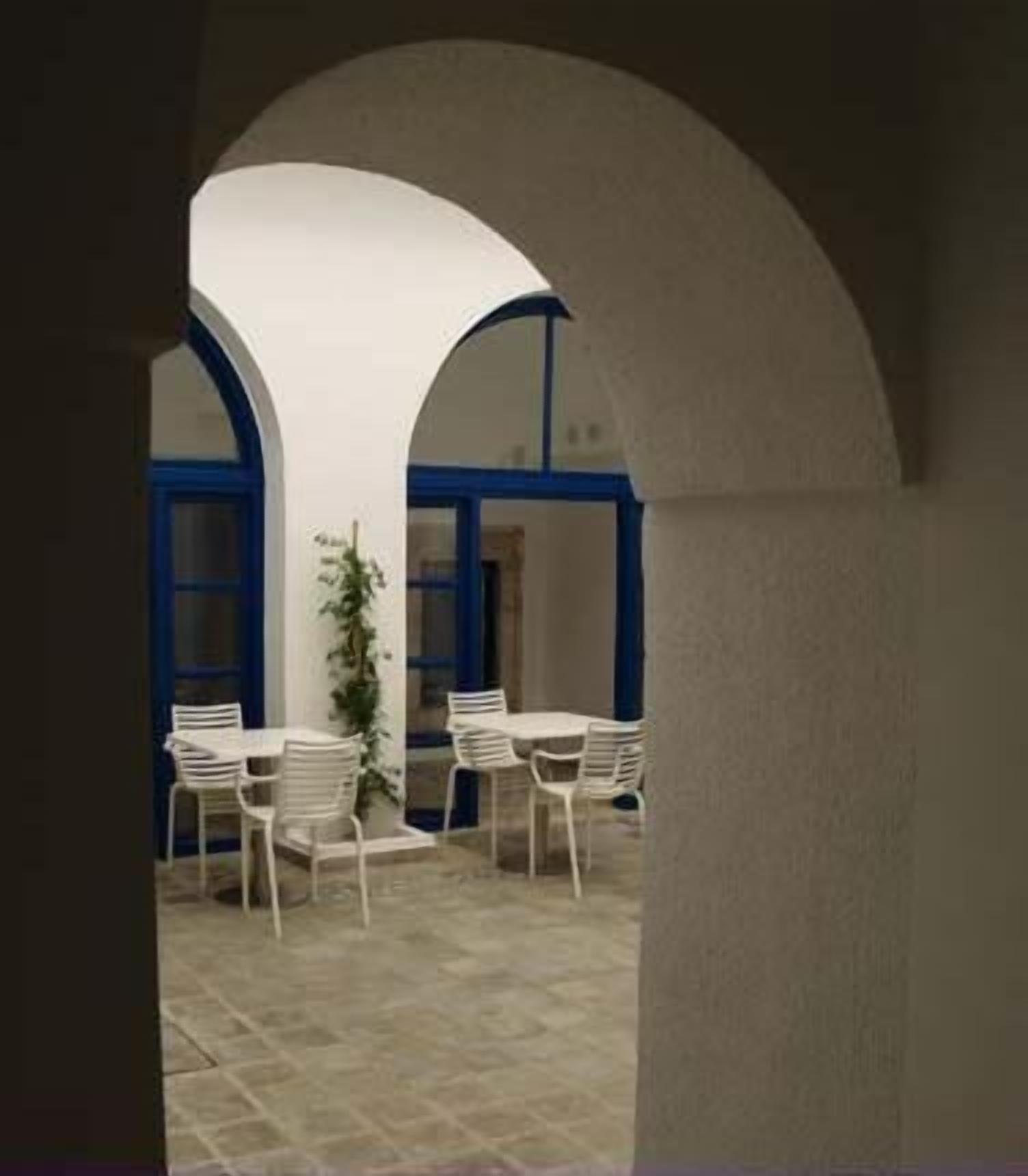 An outdoor seating area with white chairs and tables, surrounded by white walls and blue accents.
