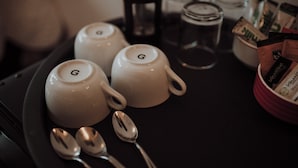 A tray with two white teapots marked with the letter 'G', two spoons, and a red container holding tea bags. - 16 Pilrig Guest House (Edinburgh)