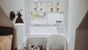 A small, neatly arranged room with a single window, a white chair, a small table, and a lamp. - 16 Pilrig Guest House (Edinburgh)