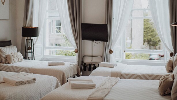 A hotel room with two beds, a desk, a chair, a television, and a chandelier. - 16 Pilrig Guest House (Edinburgh)