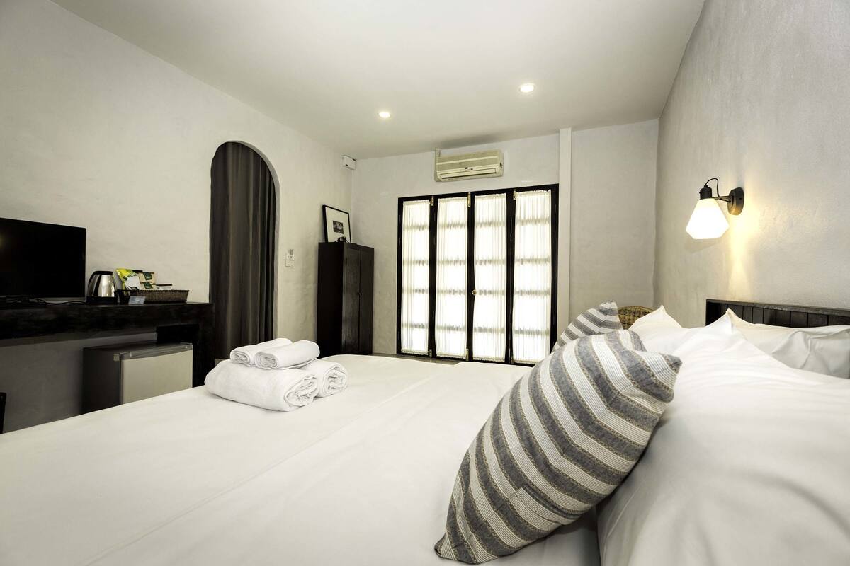 A hotel room with a bed, a TV, a desk, a refrigerator, and a window with curtains.
