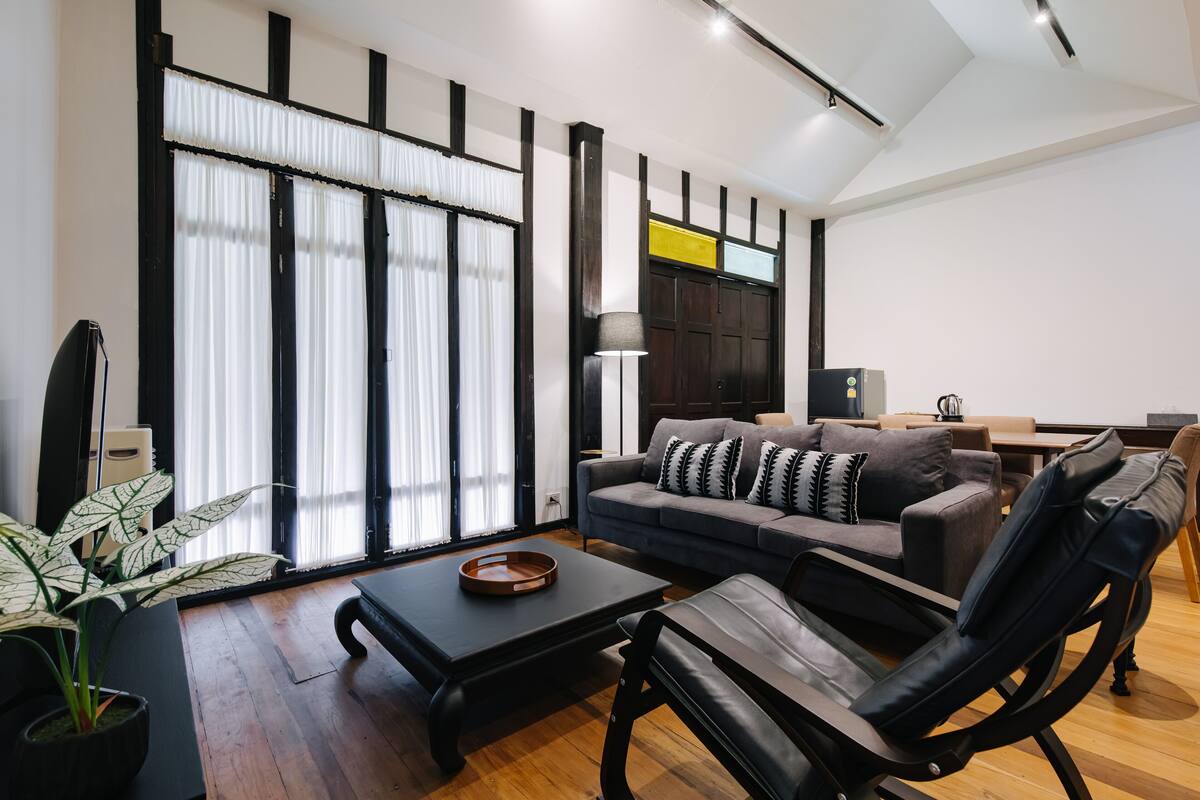 A modern living room with a sofa, coffee table, and a chair. There is a plant, a lamp, and a window with curtains.