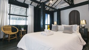 A hotel room with a large bed, a chair, a small table with a plant, and a nightstand with a lamp. - Chotana Villa (Chiang Mai)