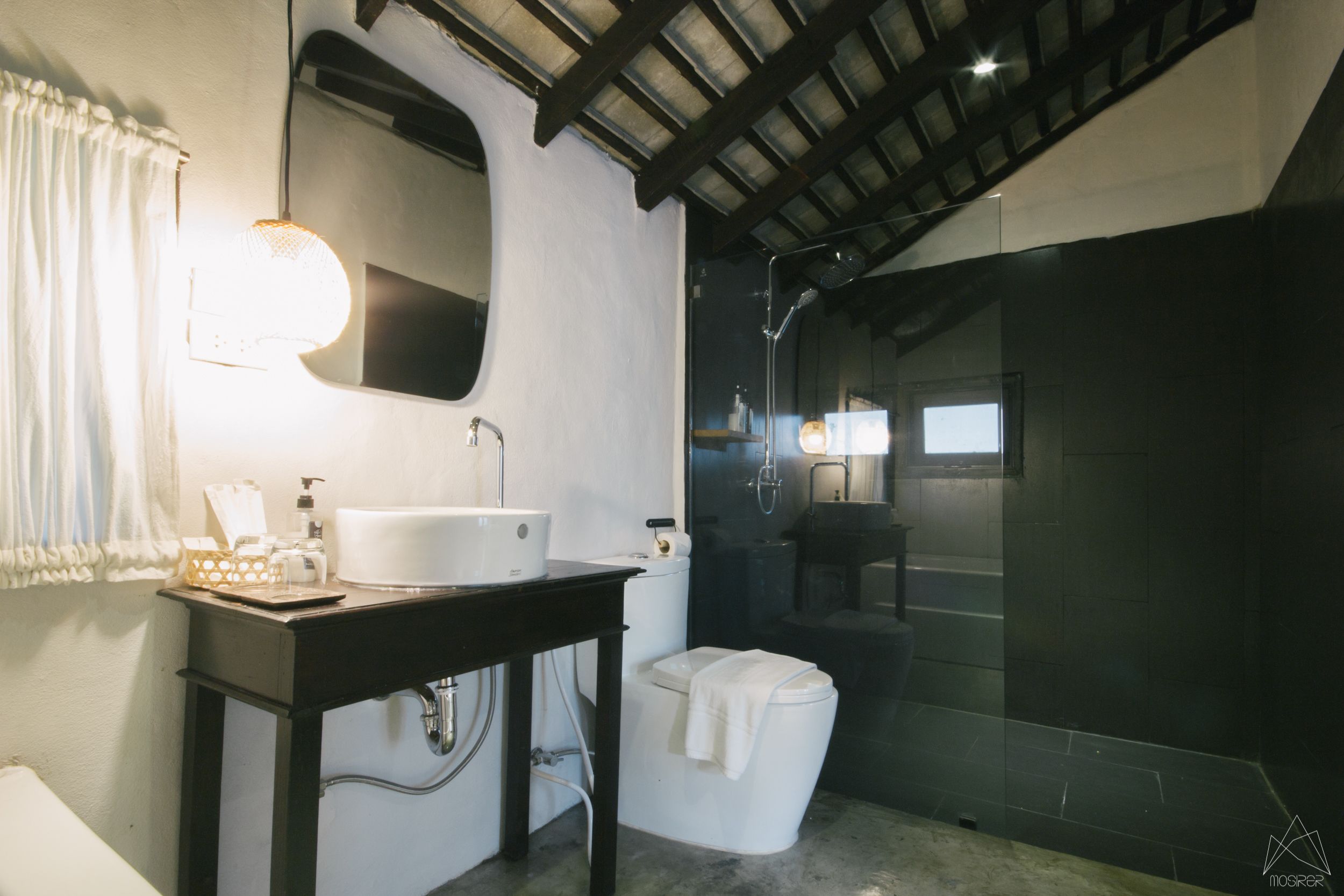 A modern bathroom with a white sink, mirror, and toilet. There is a shower area with glass doors and a towel hanging on the toilet.