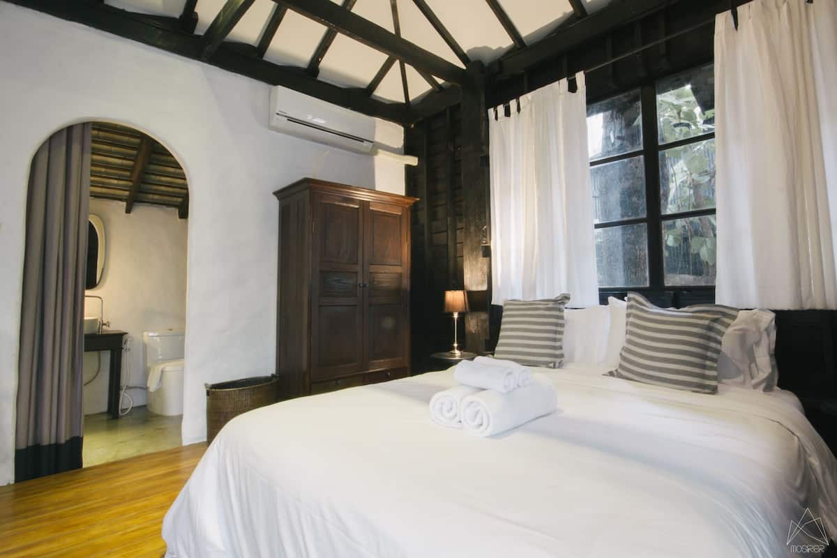 A hotel room with a large bed, wooden wardrobe, and a window with curtains.