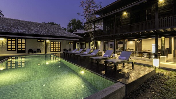 A swimming pool with lounge chairs and a wooden deck, surrounded by traditional architecture. - Chotana Villa (Chiang Mai)
