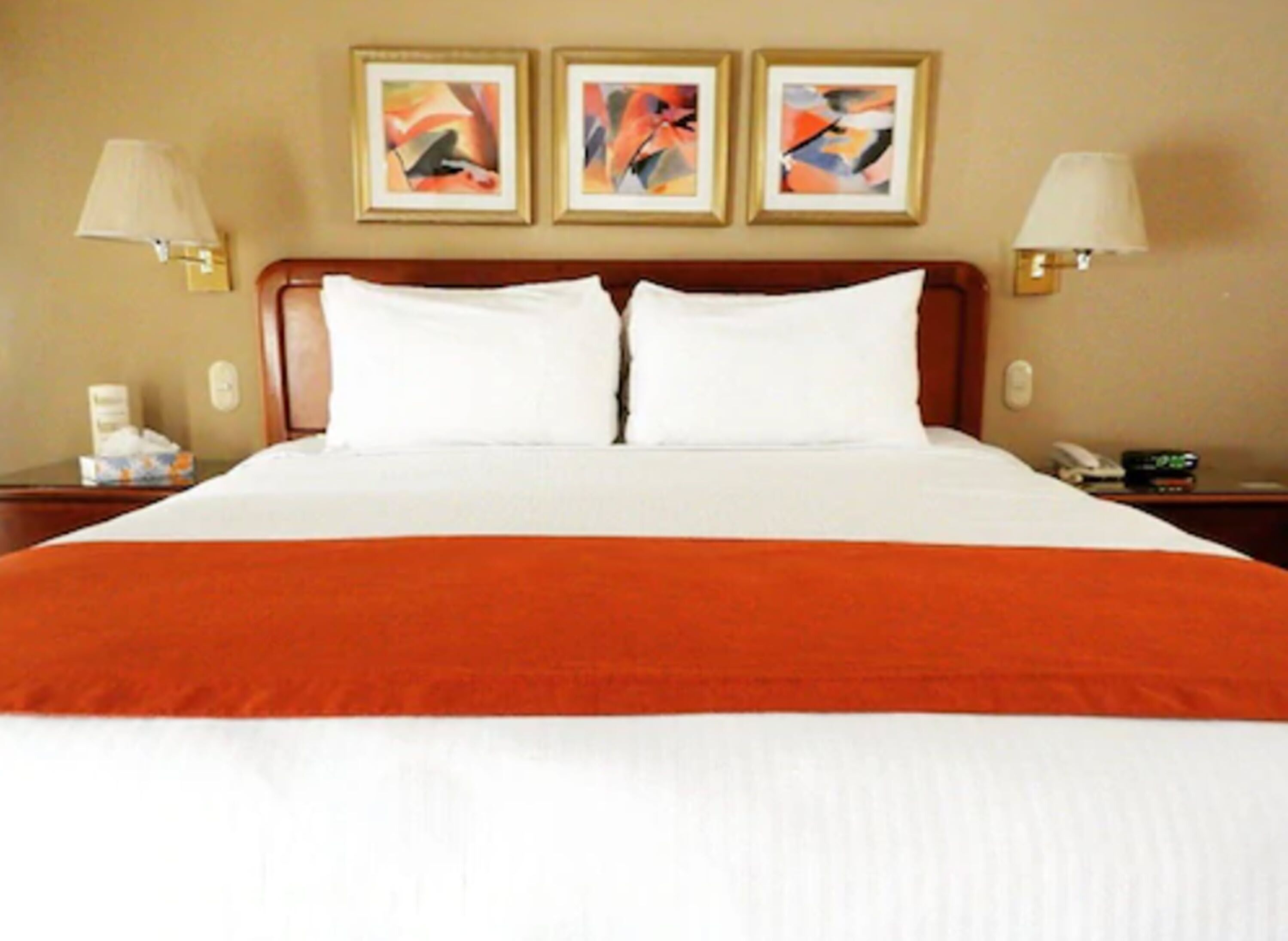 Ein Hotelzimmer mit einem großen Bett, zwei Nachttischen und drei gerahmten abstrakten Bildern an der Wand.