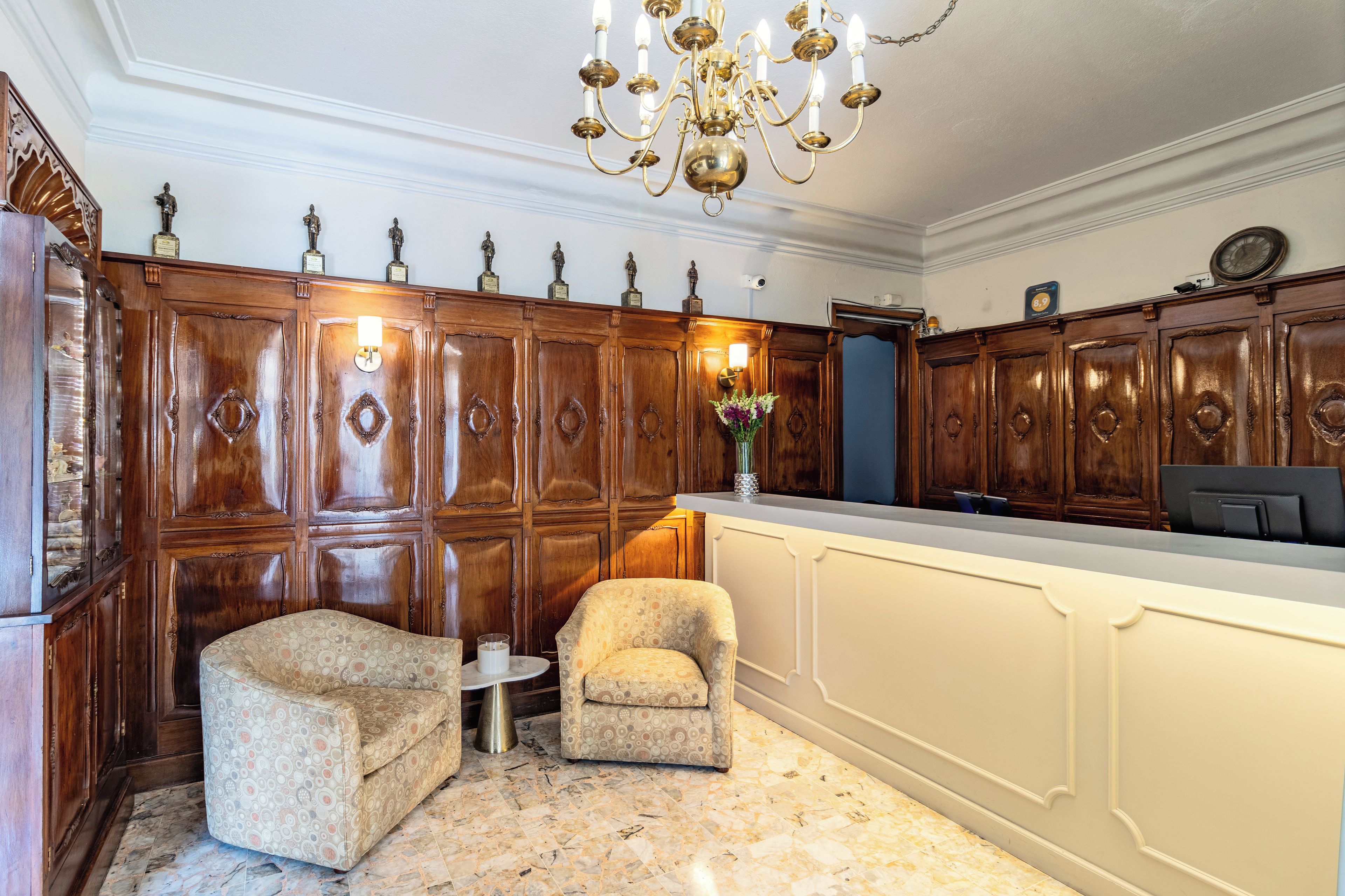 A room with a wooden panel wall, a chandelier, a desk, and two armchairs.