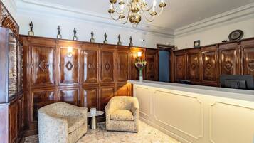 A room with a wooden panel wall, a chandelier, a desk, and two armchairs.