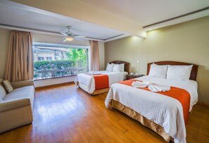 Une chambre d’hôtel avec deux lits, un canapé et un balcon donnant sur un espace verdoyant.