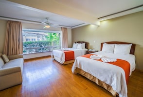 Habitación de hotel con dos camas, un sofá y un balcón con vistas a zonas verdes.