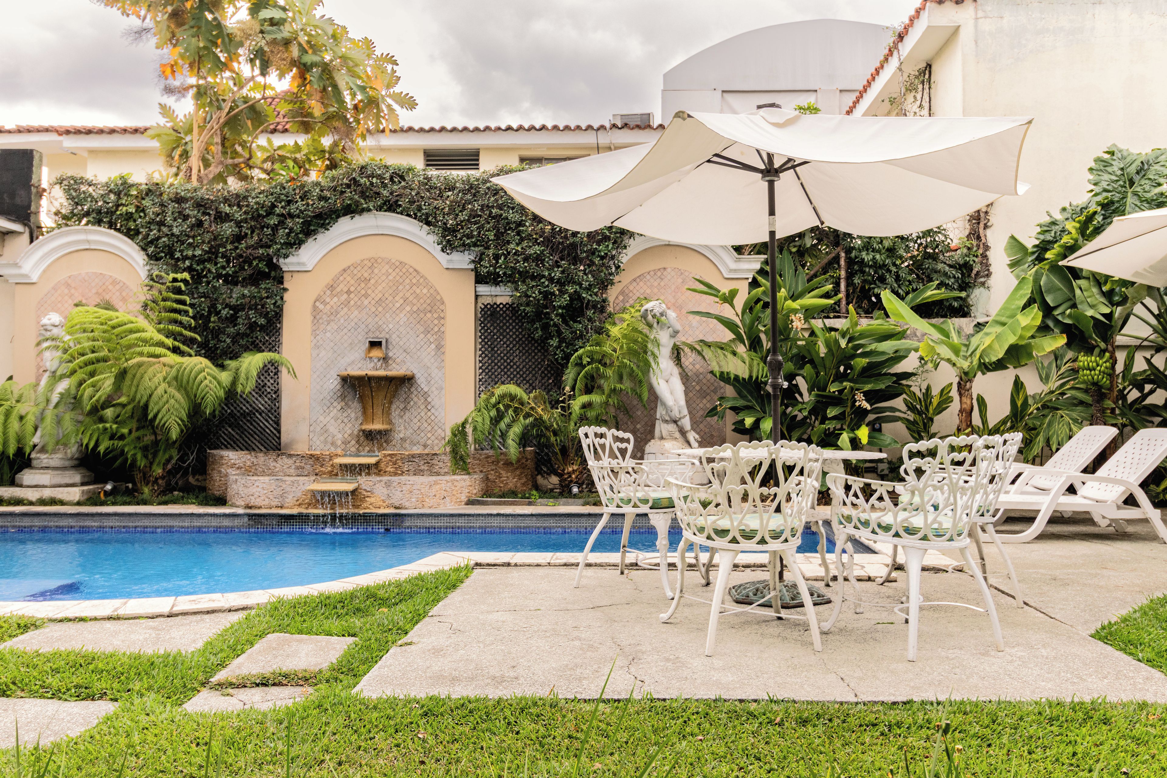 A poolside area with a fountain, lounge chairs, and umbrellas.