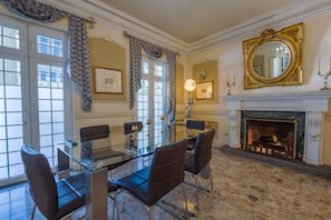 A formal dining room with a glass table, leather chairs, a fireplace, and decorative curtains. - Hotel San Carlos (Guatemala City)