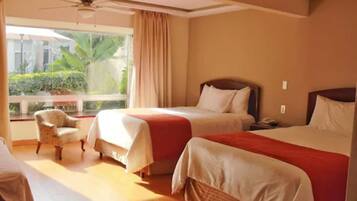 Habitación de hotel con dos camas, una silla y un ventanal con vistas a zonas verdes.