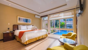 Habitación de hotel con cama, una mesita, sillas amarillas, televisión y vista a una piscina.
