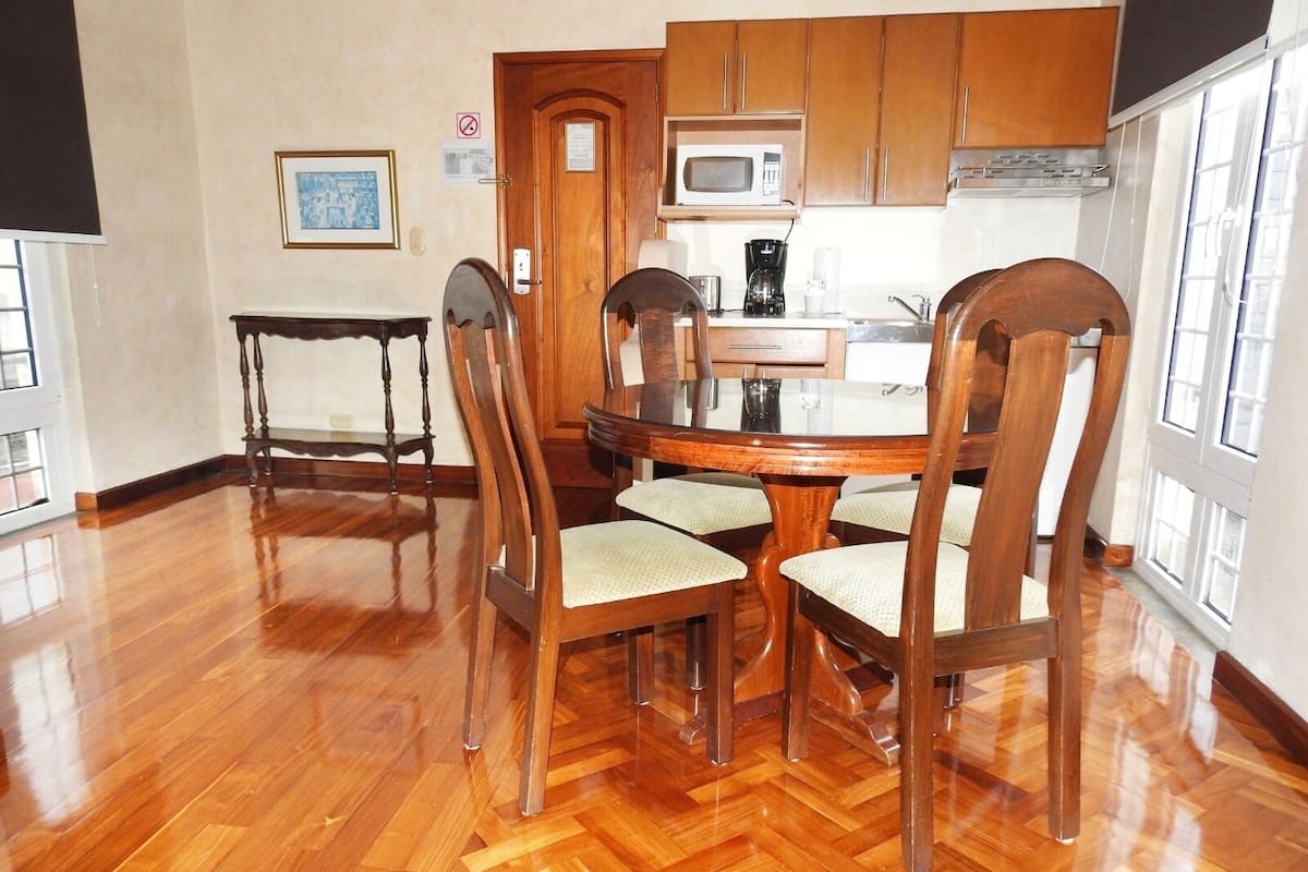Een eetgedeelte met een houten tafel en stoelen, een keuken met een magnetron, en een deur met een bordje.