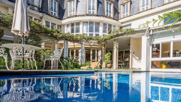 Un patio de hotel con piscina, mobiliario exterior y un edificio de múltiples ventanas y una torre.
