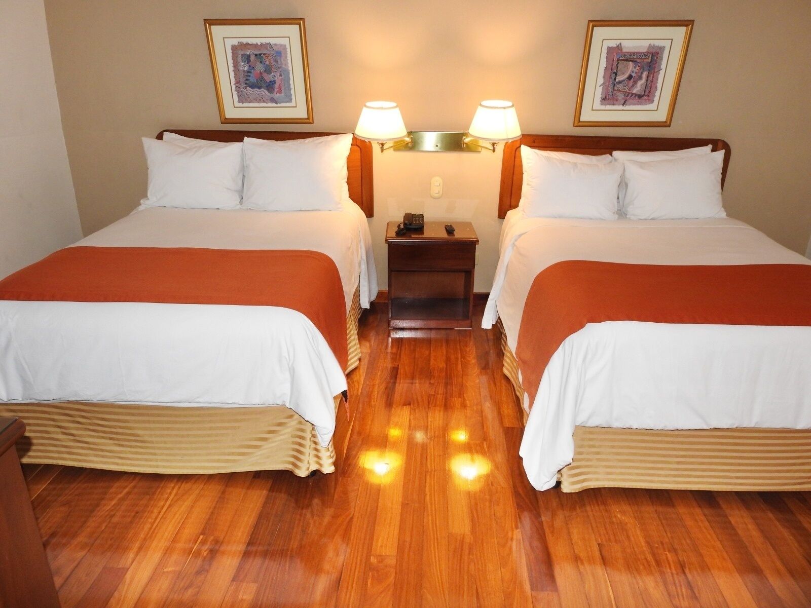 Habitación de hotel con dos camas, piso de madera y cuadros en las paredes.