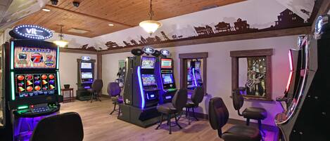 A gaming area with multiple slot machines, chairs, and a wooden ceiling.
