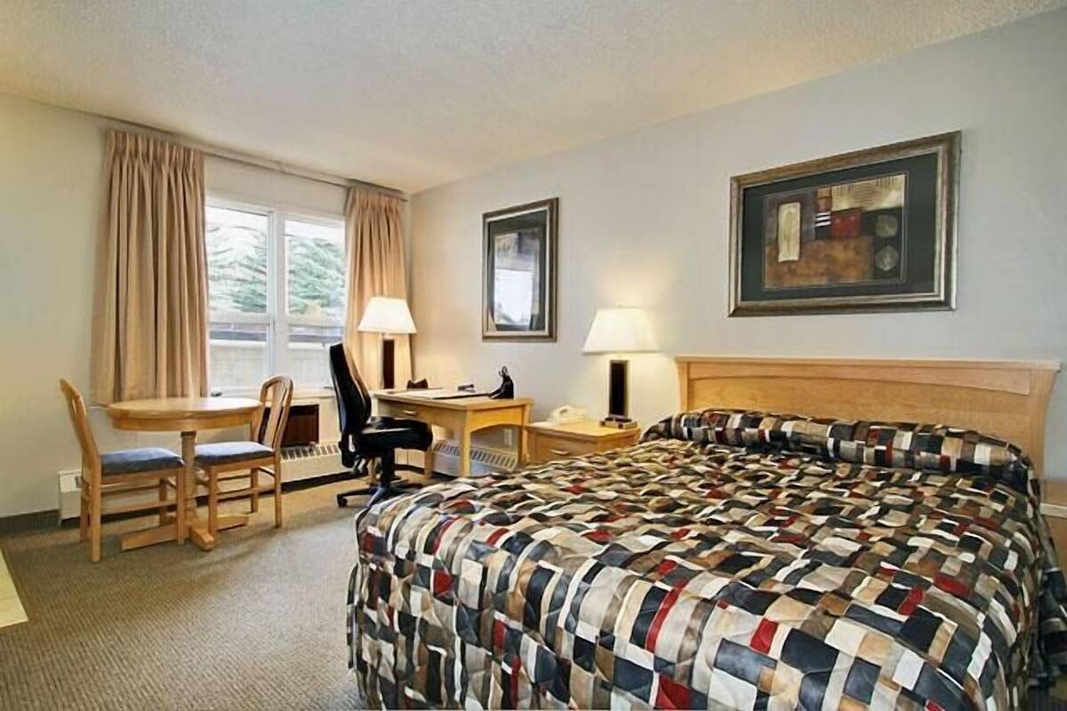 Hotellihuone, jossa on sänky, työpöyt ä, tuoli ja kaksi lamppua.