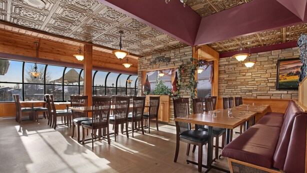 A restaurant with wooden tables and chairs, a stone wall, and large windows. - Guest House Inn & Suites (Edson)