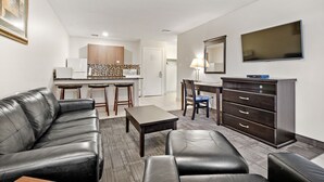 A modern living room with a black leather sofa, a coffee table, a TV, and a dark wooden dresser. - Guest House Inn & Suites (Edson)