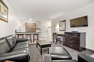 A modern living room with a black leather sofa, a coffee table, a TV, and a dark wooden dresser.