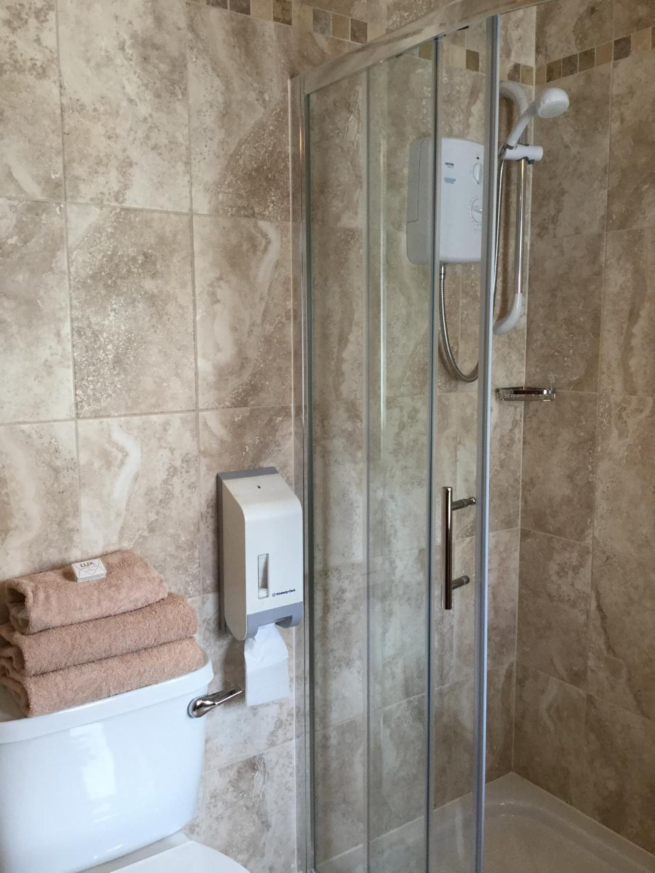 A bathroom with a glass-enclosed shower, a toilet, and a paper towel dispenser.